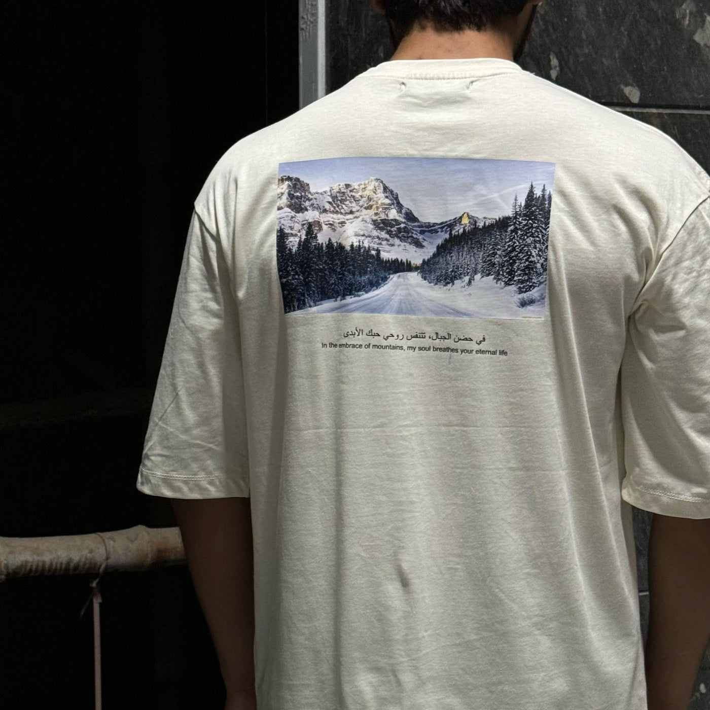 A person wearing an oversized white t-shirt with a mountain range print on the back.